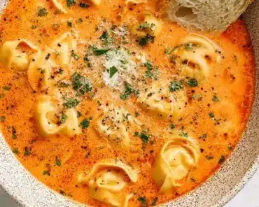 Bowl of rich tomato tortellini soup garnished with fresh herbs